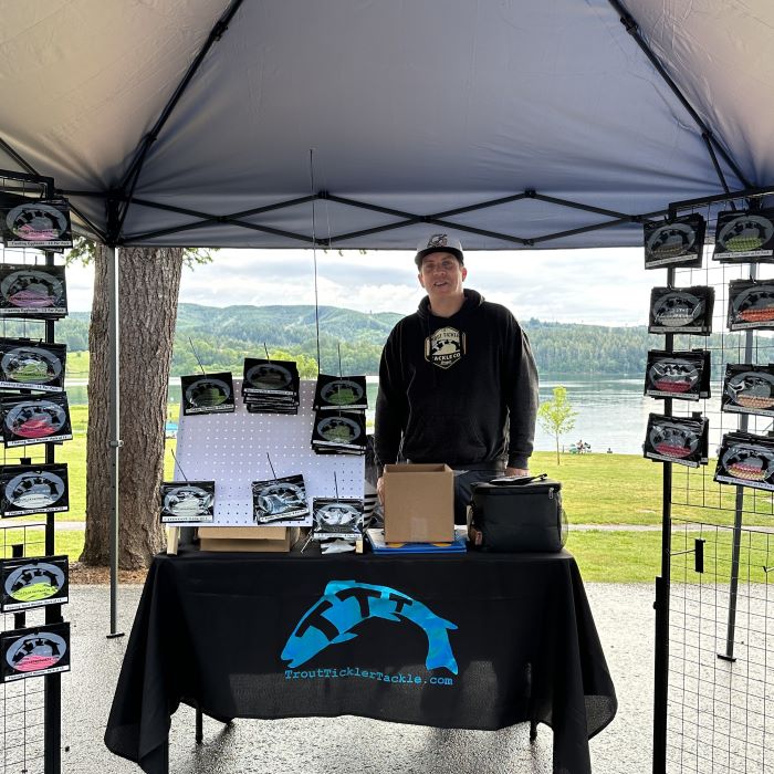 A man stands behind a table in a trout Tickler Tackle merchandise booth